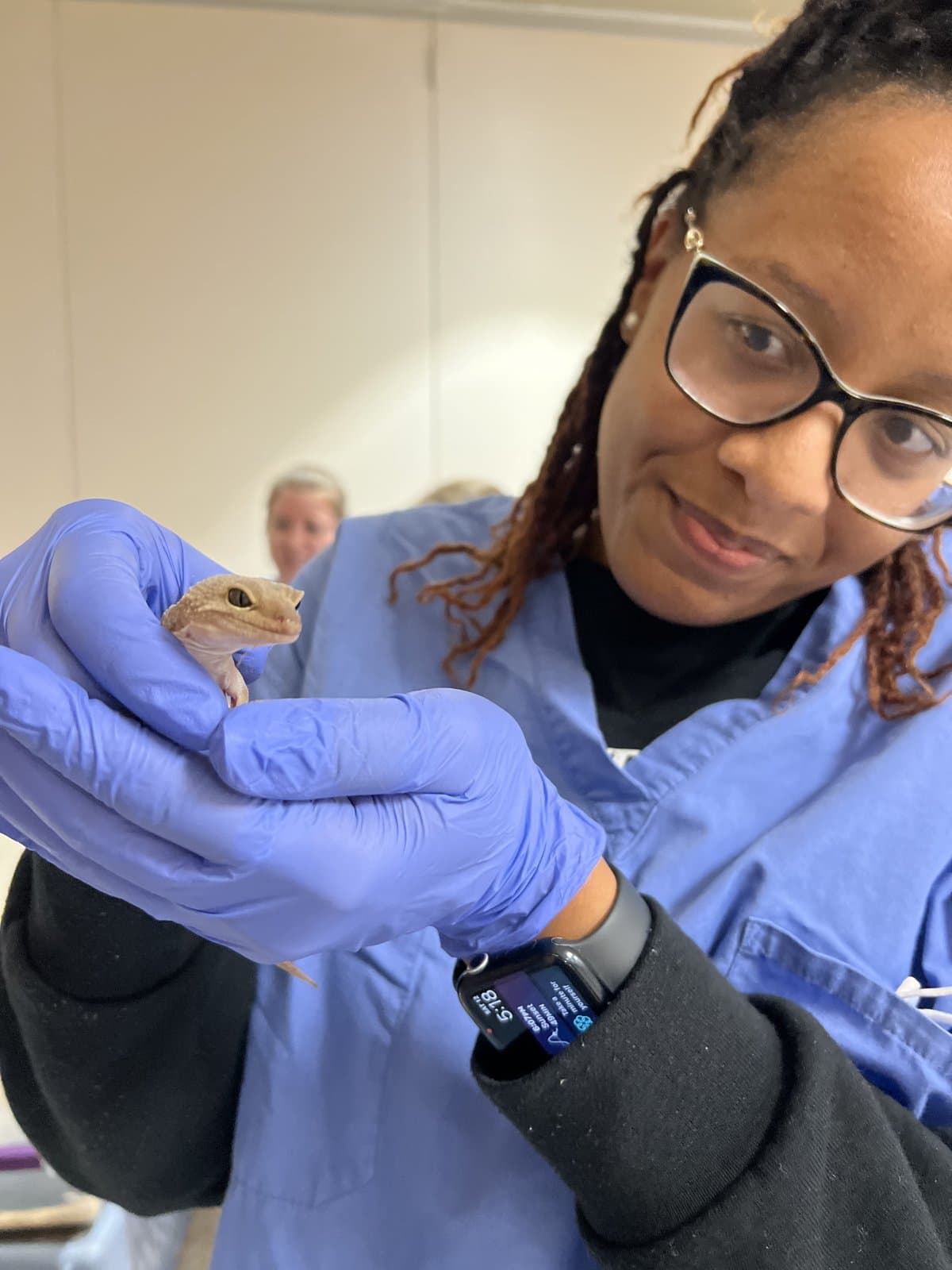Dr. Aisha Ellis smiling at a small reptile patient she's gently holding in gloved hands